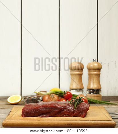 A piece of raw beef and rosemary on the kitchen table
