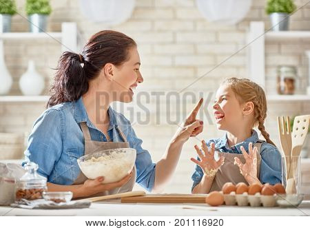 Happy loving family are preparing bakery together. Mother and child daughter girl are cooking cookies and having fun in the kitchen. Homemade food and little helper.