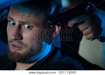 Closeup of dangerous criminal person pointing gun at the driver. Car theif threatening frightened driver, night time.