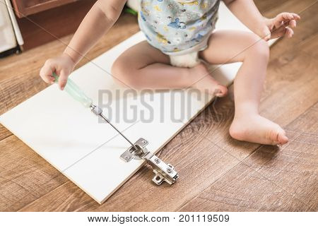 Baby holds a screwdriver and repairs the cabinet door