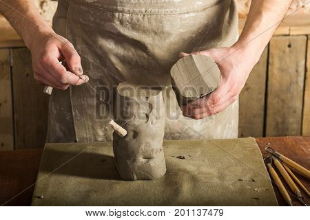 potter, clay workshop, ceramics art concept - closeup on hands of male ceramist, standing man cut off the part of raw fireclay with the string cutter, wooden table with sculpting tools set