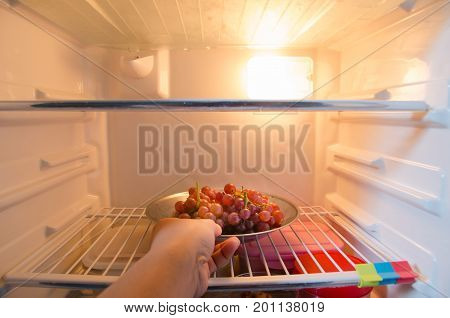 Hand reaches for a plate of graps in refrigerator