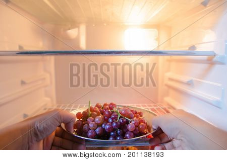 Hand reaches for a plate of graps in refrigerator