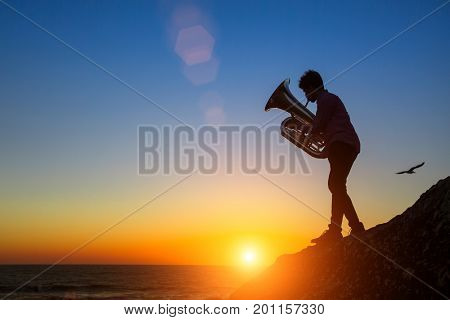 Silhouette of man play Tuba on sea shore at amazing sunset.