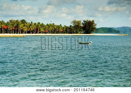 Fishing boat rowing alone in the middle of a bay with an island in the background. Perfect for a shipwrecked representation or a place to unwind