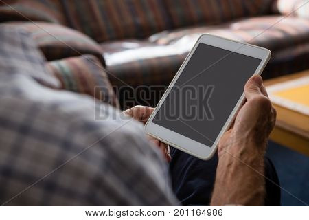 Cropped hands of senior man using tablet computer while sitting in nursing home