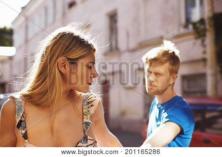 Quarrel between young lovers strolling on city streets. Beautiful girl witn nose ring having unhappy sad look leaving her boyfriend after she learned about his infidelity. Relationships problems