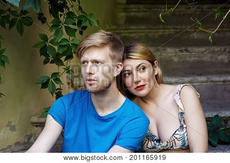 Dating love romance and youth concept. Outdoor portrait of serious young Caucasian woman with facial piercing wearing floral cropped top relaxing in shadow with her confident blonde boyfriend