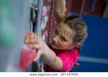 Determined teenage girl practicing rock climbing in fitness studio