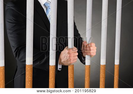 Midsection of businessman holding big cigarettes while wearing handcuffs against black background