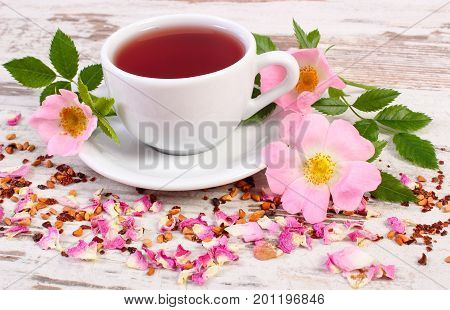 Cup Of Hot Tea With Wild Rose Flower On Old Rustic Wooden Board
