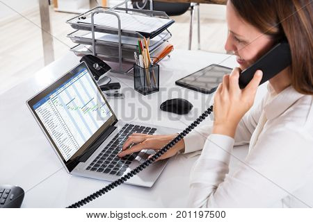 Happy Young Businesswoman Talking On Landline Phone With Gantt Chart On Laptop Screen