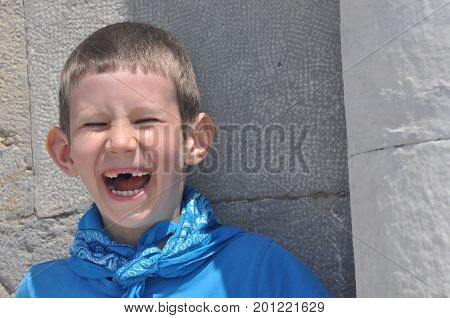 A gloomy boy with milk teeth in a shirt and a bandage laughing on a sunny day.