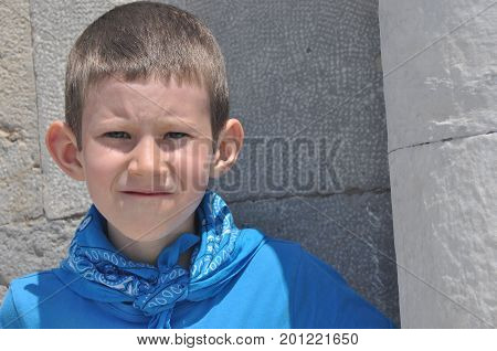 A gloomy boy with milk teeth in a shirt and a bandage laughing on a sunny day.