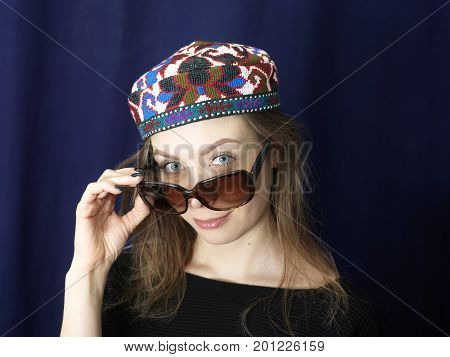 A young woman in colorful hat with inquisitive look over the sunglasses. Studio portrait