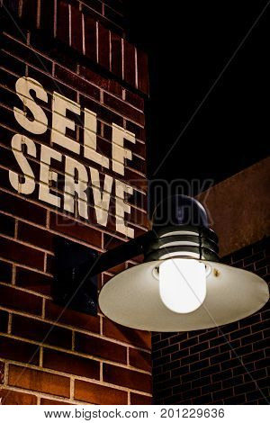 self serve sign on brick wall with light vertical