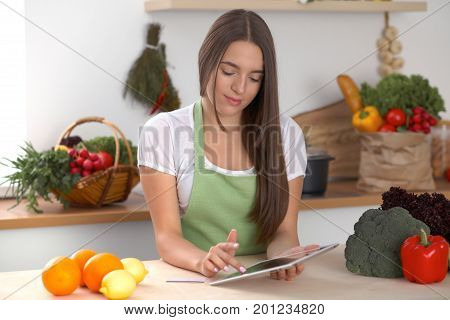 Young  woman is making online shopping by tablet computer and credit card. Housewife found new recipe for  cooking in a kitchen.