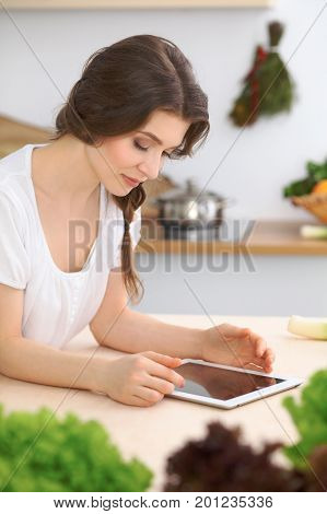 Young  woman looking for a new recipe for  cooking in a kitchen. Housewife is making online shopping by tablet computer and credit card.