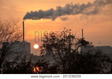 Horizon Industry In A Small Netherland Town In Europe, With A Big Chimney And Smoke, Sunset And Sun