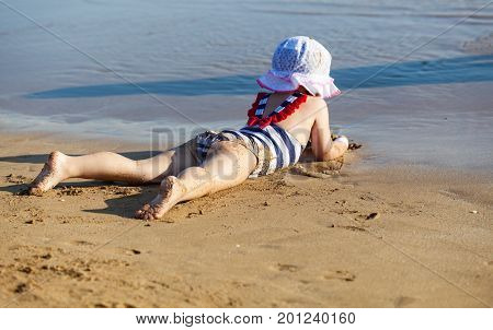 Happy little girl lying on the sand on the beach of sea