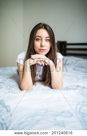 Woman Lying At The End Of The Bed Looking Forward And Smiling. Her Hand Against Her Chin With Her Ot
