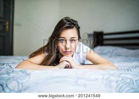 Young Woman Lying At The End Of The Bed Smiling, With Her Head Resting Upon Her Hand With The Other