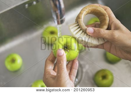 Young Vegan Girl Washing Green Apples with Bamboo Brush. Hand Holding Fresh Fruits Under Running Water in Kitchen Sink. Healthy Lifestyle Hygiene Concept