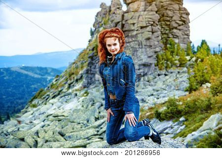 beautiful brunette girl in black clothes posing on a huge rock among stones