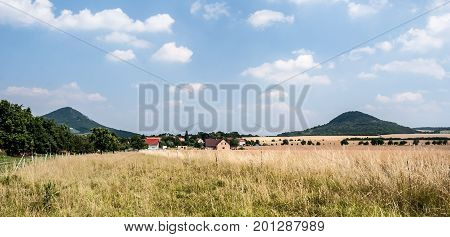 countryside with meadow field Brezno village trees isolated hills of Ceske stredohori mountain range and blue sky with clouds in Czech republic