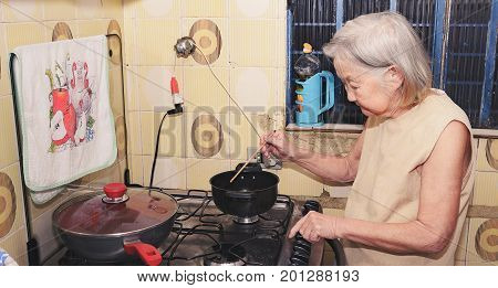 Old Woman With White Hair At Kitchen Using A Hashi