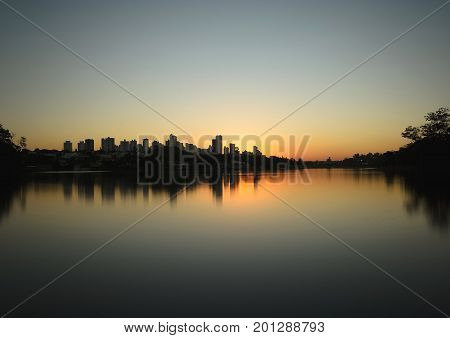 Londrina Brazil - July 24 2017: Sunset at Lago Igapo lake localized in Londrina city. The city silhouette and the water of the lake reflecting the sunset.
