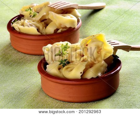 Delicious Meat Cappelletti with Herbs in Ceramic Bowls with Wooden Forks closeup on Green Napkin background