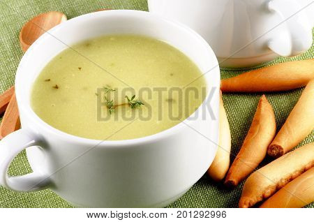 Delicious Cream Asparagus Soup in White Soup Cup with Bread Sticks and Wooden Spoon closeup on Green Napkin
