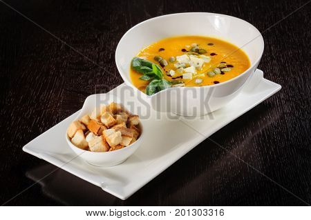 Pumpkin soup with cream and pumpkin seeds on dark wooden background. Copy space.
