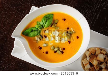 Pumpkin soup with cream and pumpkin seeds on dark wooden background. Copy space.