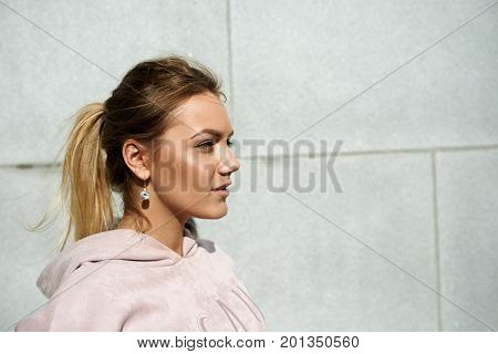 Profile portrait of positive and carefree young blonde European woman with perfect tanned sking and blonde hair gathered in ponytail standing isolated against blank copyspace wall background