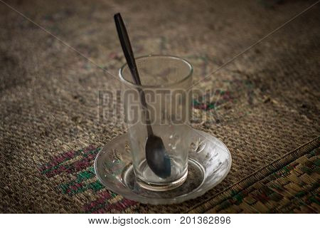 an empty glass on top of traditional mat with spoon java