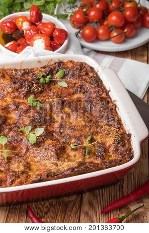 Fresh Baked Lasagne in Red Dish with Black Olives Tomatoes and Chilli on Wooden Table with Herbs and Pepper