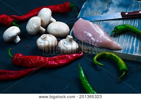 raw chicken wings with herbs in a transparent bowl Cauliflower with tomatoes and herbs and hot peppers with mushrooms on wooden background top view close up.