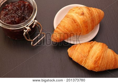 French Croissant with jam jar on black background