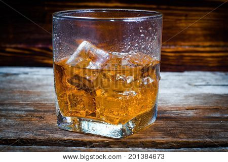 Two glasses of whiskey with ice cubes served on wooden planks. Vintage countertop with highlight and a glass of hard liquor