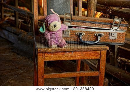 closed old suitcase with a plush toy stand on an old wooden chair