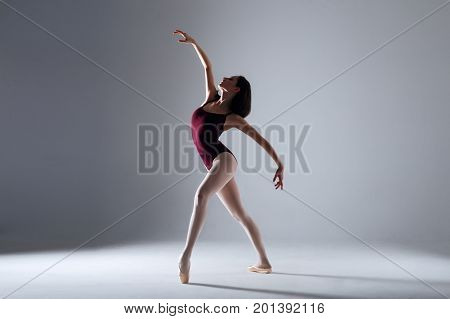 Slim ballerina is dancing in the white studio in the contrast light
