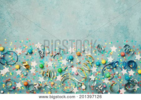 Holiday background decorated colorful confetti star candy and streamer on blue vintage table top view. Flat lay style. Festive border with copy space.