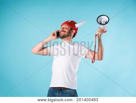 The football fan with megaphone over blue. The young man looking at camera with different emotions on face