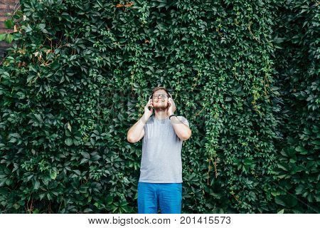 man stands in front of building in ivy and listins music concept