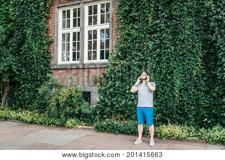 man stands in front of building in ivy and listins music concept