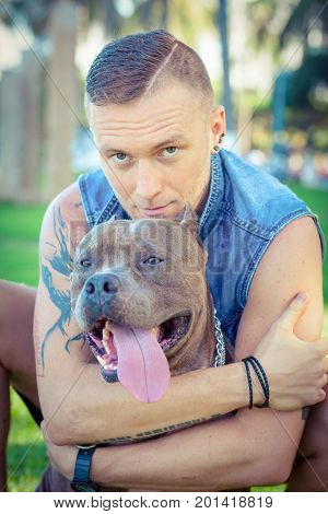 Man and dog american pit bull terrier relaxing at the park embracing and hugging. Caucasian male with strong dog