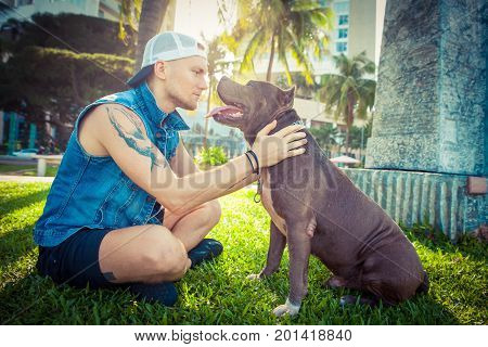 Man and dog american pit bull terrier relaxing at the park embracing and hugging. Caucasian male with strong dog