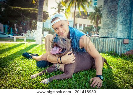 Man and dog american pit bull terrier relaxing at the park embracing and hugging. Caucasian male with strong dog